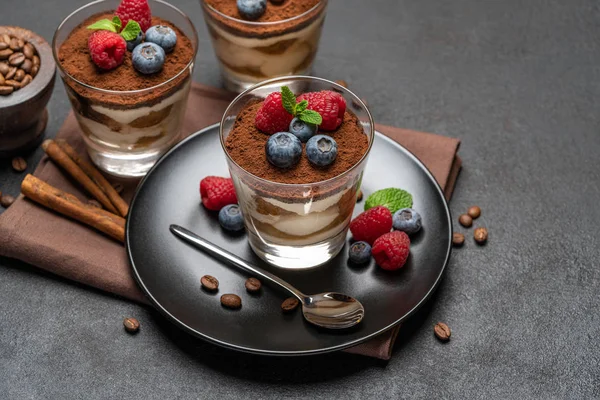 Dessert tiramisù classico con mirtilli e lamponi in un bicchiere su sfondo di cemento scuro — Foto Stock