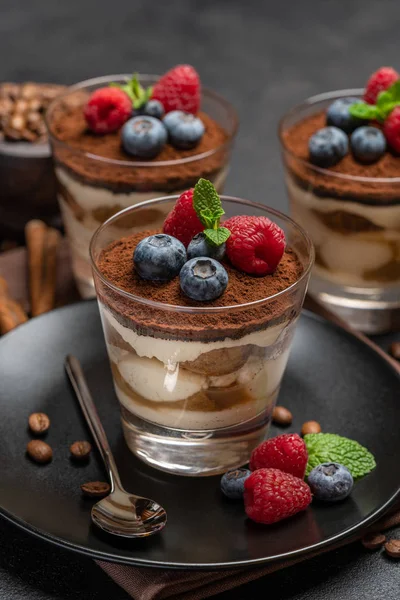 Classic tiramisu dessert with blueberries and raspberries in a glass on dark concrete background — Stock Photo, Image
