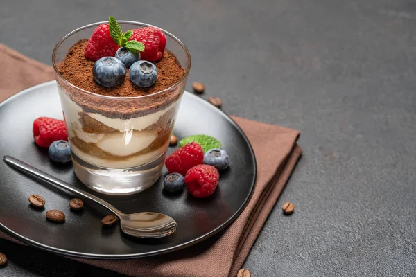 Klassiek Tiramisu-dessert met bosbessen en frambozen in een glas op een donkere betonnen achtergrond — Stockfoto