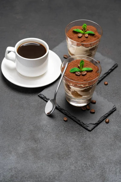 Classic tiramisu dessert in a glass on stone serving board and cup of coffee on dark concrete background — Stock Photo, Image