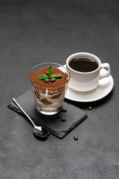 Klassisches Tiramisu-Dessert im Glas auf Steinplatte und Tasse Kaffee auf dunklem Betongrund — Stockfoto