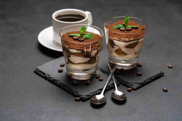 Sobremesa tiramisu clássico em um copo na placa de serviço de pedra e xícara de café no fundo de concreto escuro — Fotografia de Stock