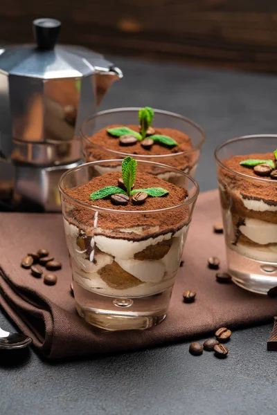 Classic tiramisu dessert in a glass and coffee maker on dark concrete background — Stock Photo, Image