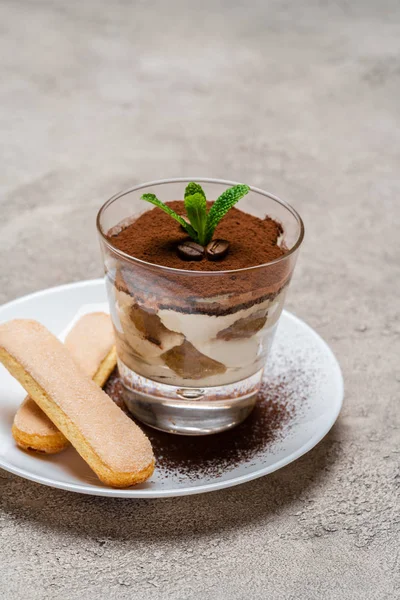 Classico dessert tiramisù in tazza di vetro e biscotti savoiardi su piatto su fondo di cemento — Foto Stock