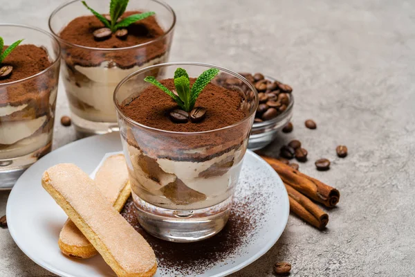 Classico dessert tiramisù in tazza di vetro e biscotti savoiardi su piatto su fondo di cemento — Foto Stock