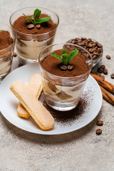 Classic tiramisu dessert in a glass cup and savoiardi cookies on plate on concrete background — Stock Photo, Image