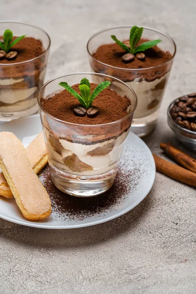 Postre tiramisú clásico en una taza de vidrio y galletas savoiardi en plato sobre fondo de hormigón — Foto de Stock