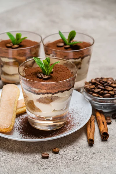 Sobremesa tiramisu clássico em uma xícara de vidro e biscoitos savoiardi na placa no fundo de concreto — Fotografia de Stock