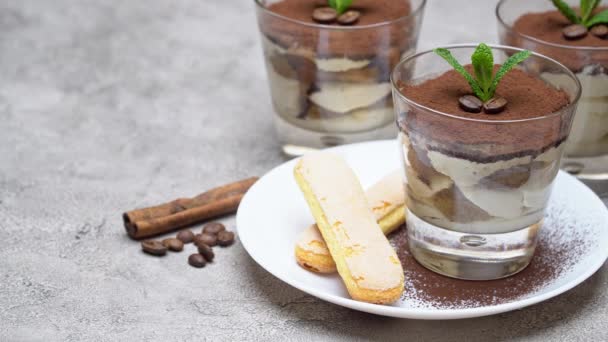 Postre tiramisú clásico en una taza de vidrio y galletas savoiardi en plato sobre fondo de hormigón — Vídeos de Stock