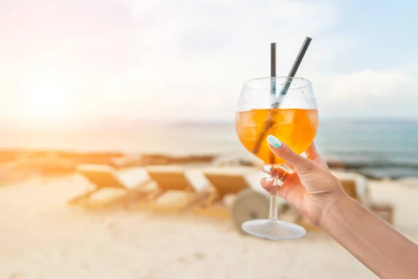 Donna che tiene Delicious classico cocktail di spritz di aperol ghiacciato con cubetti di ghiaccio su una spiaggia tropicale calda in sole estivo — Foto Stock