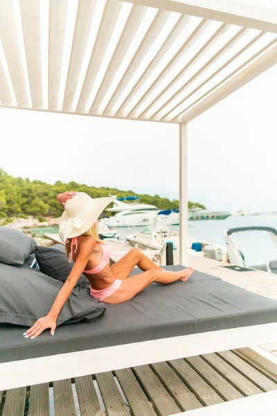 Jovem bela mulher vestindo chapéu e pareo sentado na cama de sol — Fotografia de Stock