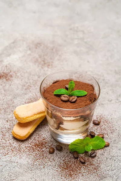 Dessert tiramisù classico in tazza di vetro e biscotti savoiardi su fondo di cemento — Foto Stock