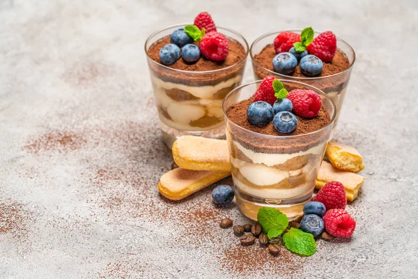 Класичний десерт тірамісу з чорницею та малиною та печивом савойді у склянці на бетонному фоні — стокове фото