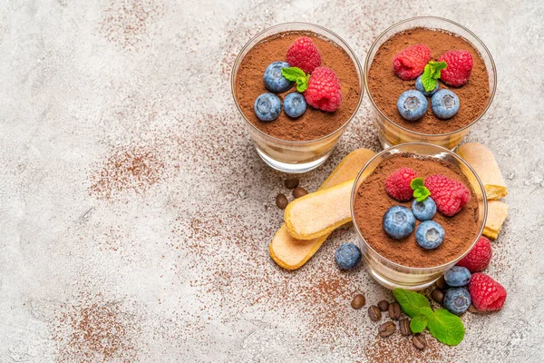 Klassisches Tiramisu-Dessert mit Blaubeeren und Himbeeren und savoiardi-Keksen im Glas auf Betongrund — Stockfoto