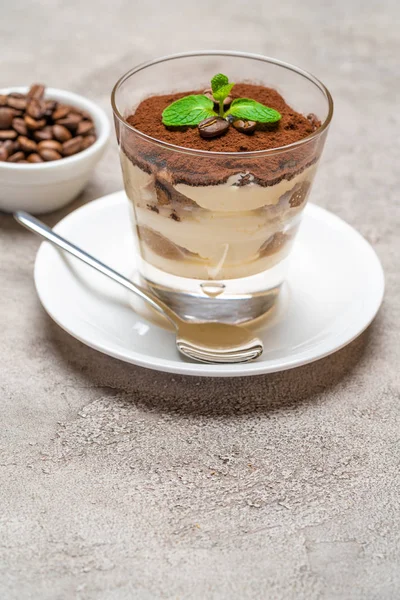 Klassisches Tiramisu-Dessert in einer Glasschale auf Teller und Kaffeebohnen auf Betongrund — Stockfoto