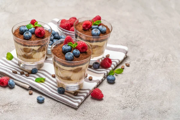 Класичний десерт тірамісу з чорницею та малиною у склянці на кухонному рушнику на бетонному фоні — стокове фото
