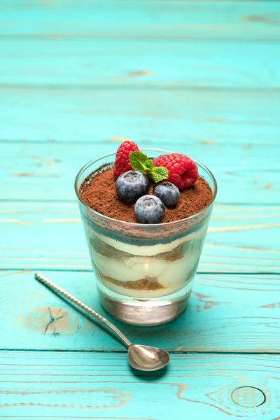 Классический десерт из тирамису с черникой и клубникой в стеклянной чашке на деревянном фоне — стоковое фото