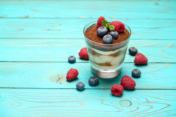 Klassisches Tiramisu-Dessert mit Blaubeeren und Erdbeeren in einer Glasschale auf Holzgrund — Stockfoto