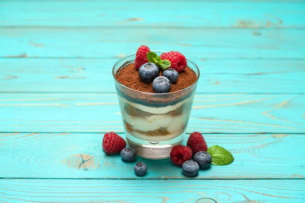 Классический десерт из тирамису с черникой и клубникой в стеклянной чашке на деревянном фоне — стоковое фото