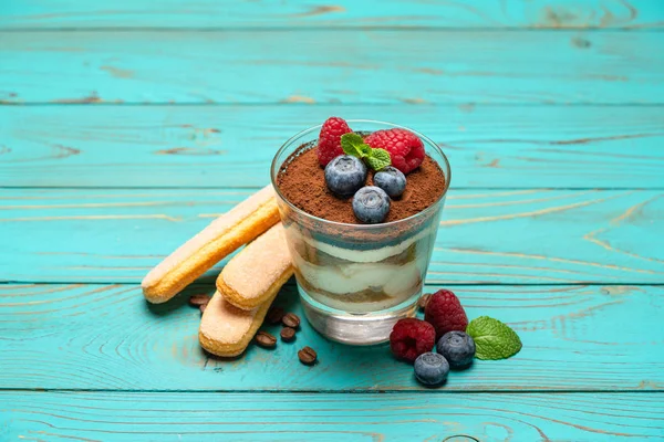 Klassisches Tiramisu-Dessert mit Blaubeeren und Erdbeeren in einer Glasschale und Savoiardi-Keksen auf Holzgrund — Stockfoto