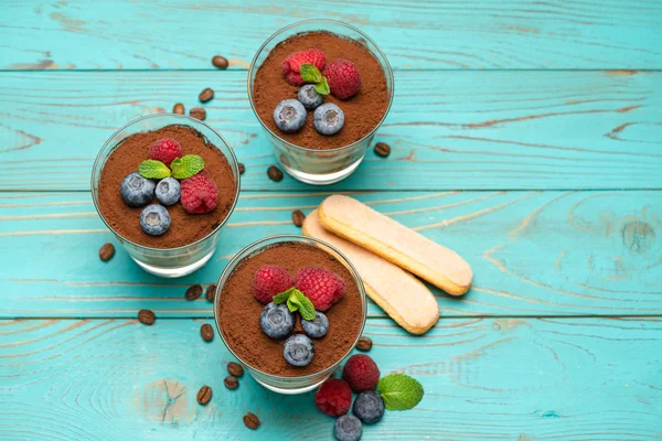 Klassisches Tiramisu-Dessert mit Blaubeeren und Erdbeeren in einer Glasschale und Savoiardi-Keksen auf Holzgrund — Stockfoto