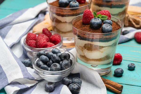 Klassiek Tiramisu-dessert met bosbessen en aardbeien in een glazen beker en Savoiardi-koekjes op houten achtergrond — Stockfoto