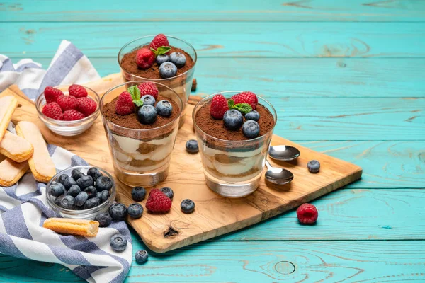 Sobremesa tiramisu clássica com mirtilos e morangos em uma xícara de vidro e biscoitos savoiardi em fundo de madeira — Fotografia de Stock