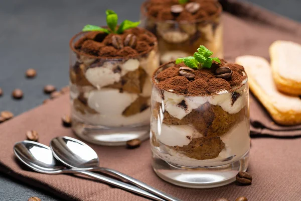 Classic tiramisu dessert in a glass cup on brown kitchen towel or napkin on dark concrete background — Stock Photo, Image
