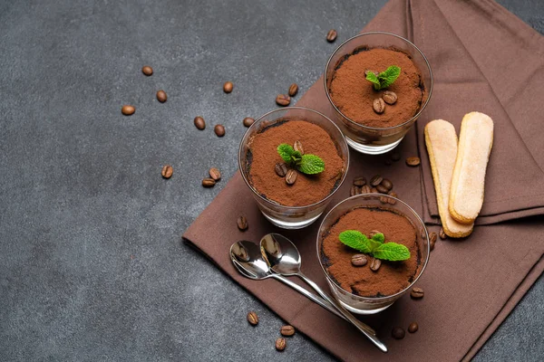 Classic tiramisu dessert in a glass cup on brown kitchen towel or napkin on dark concrete background — Stock Photo, Image