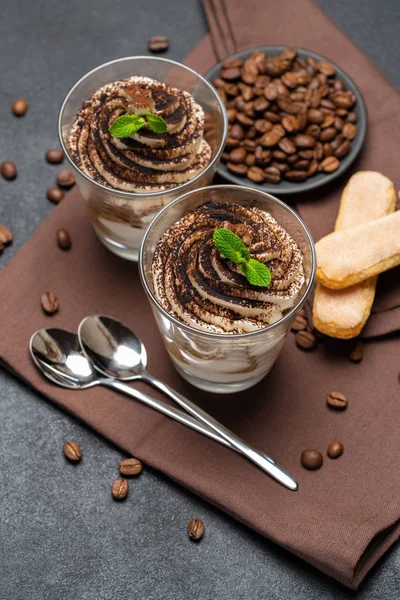 Sobremesa tiramisu clássico em uma xícara de vidro em toalha de cozinha marrom ou guardanapo no fundo de concreto escuro — Fotografia de Stock