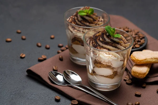 Klassisches Tiramisu-Dessert im Glasbecher auf braunem Küchentuch oder Serviette auf dunklem Betongrund — Stockfoto