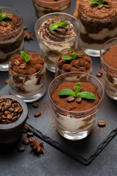 Gruppo di porzioni di dessert tiramisù classico in una tazza di vetro su tavola di pietra su sfondo di cemento — Foto Stock