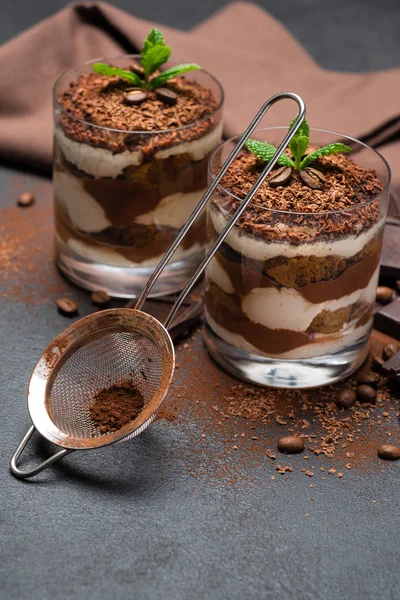 Sobremesa tiramisu clássico em uma xícara de vidro, filtro e pedaços de chocolate no fundo de concreto escuro — Fotografia de Stock
