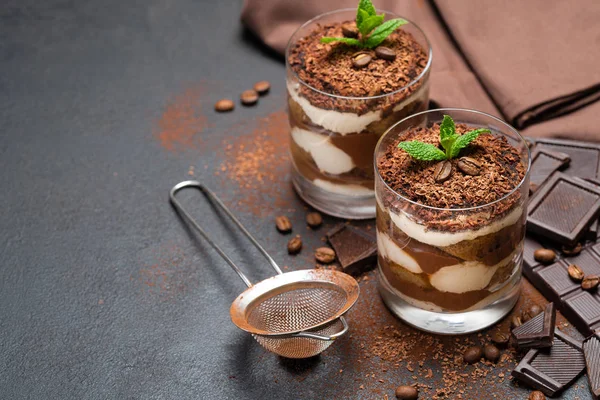 Klasszikus tiramisu desszert egy pohár csésze, szűrő és darab csokoládé a sötét beton háttér — Stock Fotó