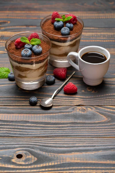 Sobremesa tiramisu clássica com mirtilos e morangos em uma xícara de vidro e café expresso em fundo de madeira — Fotografia de Stock