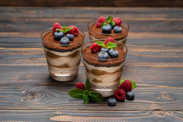 Klassisches Tiramisu-Dessert mit Blaubeeren und Erdbeeren in einer Glasschale auf Holzgrund — Stockfoto