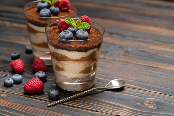 Класичний десерт тірамісу з чорницею та полуницею у склянці на дерев'яному фоні — стокове фото