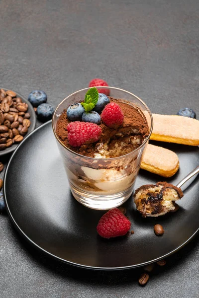 Klassisches Tiramisu-Dessertteil mit Blaubeeren und Himbeeren in einer Glasschale auf Steinplatte auf Betongrund — Stockfoto