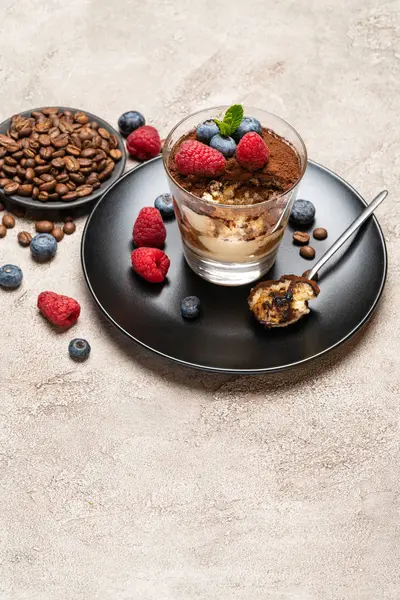 Klassisches Tiramisu-Dessertteil mit Blaubeeren und Himbeeren in einer Glasschale auf Betongrund — Stockfoto