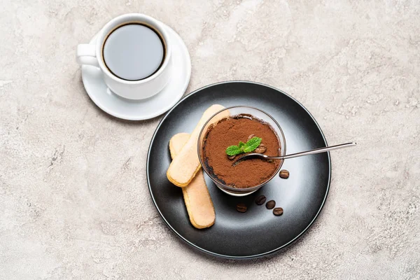 Portion de dessert tiramisu classique dans une tasse en verre, biscuits savoiardi et café expresso sur fond de béton — Photo