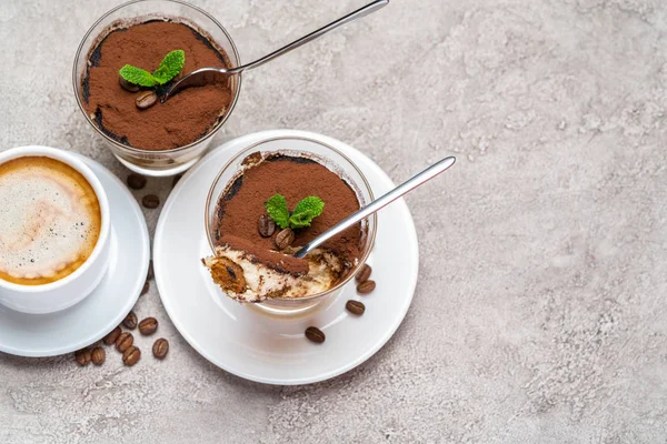 Portion de dessert tiramisu classique dans un verre et une tasse de café sur fond de béton — Photo