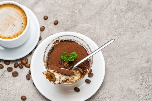 Portion de dessert tiramisu classique dans un verre et une tasse de café sur fond de béton — Photo