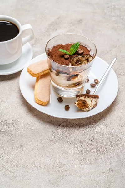 Portie klassiek Tiramisu dessert in een glas, Savoiardi koekjes en kopje koffie op concrete achtergrond — Stockfoto