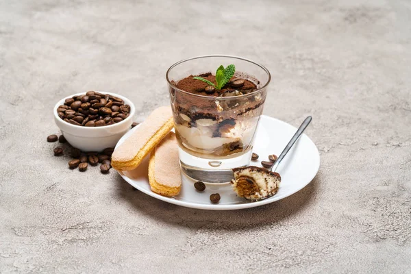 Porção de sobremesa tiramisu clássico em um copo, biscoitos savoiardi e xícara de café no fundo de concreto — Fotografia de Stock