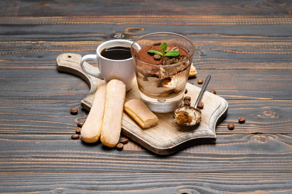 Porção de sobremesa tiramisu clássico em um copo, xícara de café e biscoitos savoiardi em fundo de madeira — Fotografia de Stock