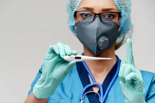 Doctora con estetoscopio con máscara protectora y guantes de látex sobre fondo gris claro que sostiene el termómetro —  Fotos de Stock