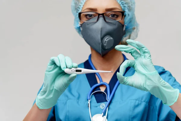 Vrouwelijke arts met stethoscoop dragen beschermende masker en latex handschoenen over lichtgrijze achtergrond houden thermometer — Stockfoto