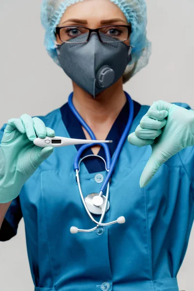 Врач-женщина со стетоскопом в защитной маске и латексных перчатках на светло-сером фоне с термометром — стоковое фото