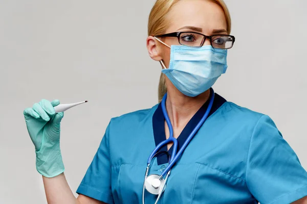 Vrouwelijke arts met stethoscoop dragen beschermende masker en latex handschoenen over lichtgrijze achtergrond houden thermometer — Stockfoto