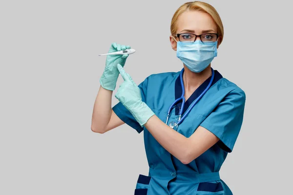 Femme médecin avec stéthoscope portant un masque protecteur et des gants en latex sur fond gris clair tenant thermomètre — Photo